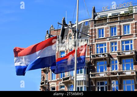 Flaggen der Niederlande winken auf dem Hintergrund des Luxushotels de L`Europe Amsterdam. Stockfoto